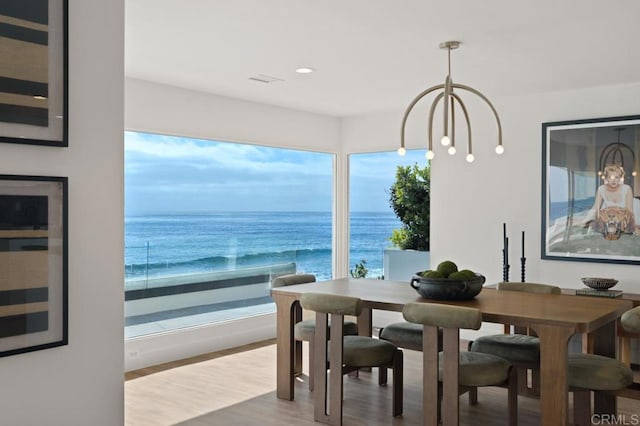 dining space with a water view, a notable chandelier, wood-type flooring, and a beach view