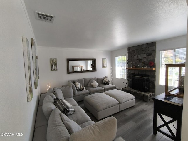 living room featuring a stone fireplace, a wealth of natural light, dark hardwood / wood-style flooring, and ornamental molding