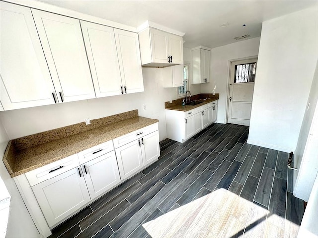 kitchen featuring light stone counters, white cabinetry, and sink