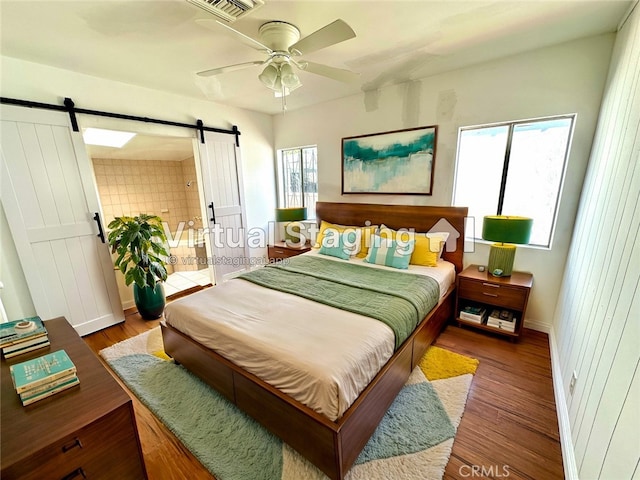 bedroom featuring a barn door, ceiling fan, dark wood-type flooring, and multiple windows