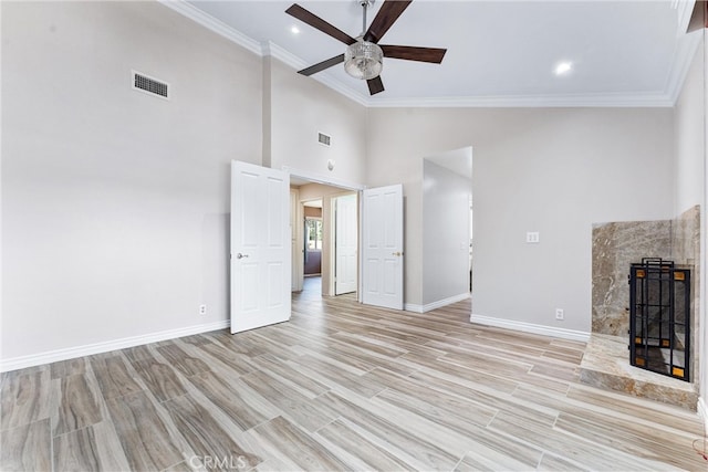 unfurnished living room featuring ceiling fan, a premium fireplace, high vaulted ceiling, crown molding, and light hardwood / wood-style floors