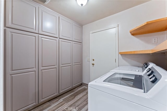 laundry room featuring cabinets, light wood-type flooring, and washer and clothes dryer