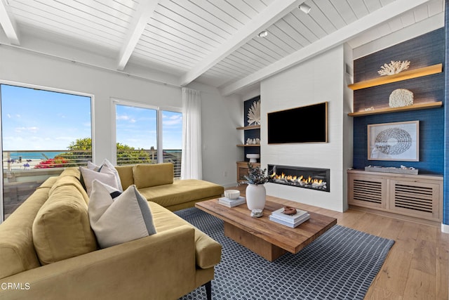 living room featuring light hardwood / wood-style floors, a water view, wooden ceiling, beam ceiling, and a large fireplace