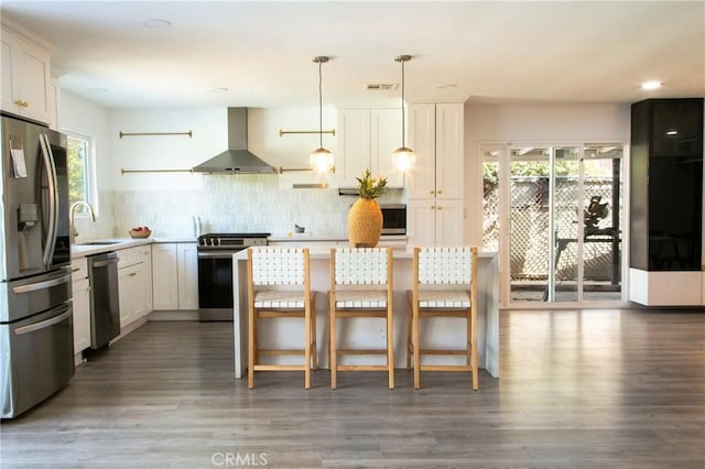 kitchen featuring pendant lighting, dark wood-type flooring, wall chimney exhaust hood, appliances with stainless steel finishes, and white cabinetry