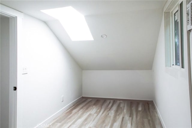 additional living space featuring vaulted ceiling with skylight and light wood-type flooring