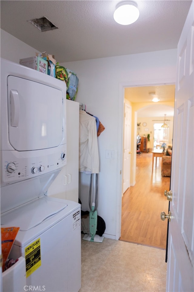 clothes washing area with light hardwood / wood-style floors, stacked washer / drying machine, and a textured ceiling