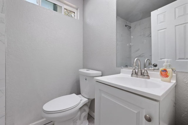 bathroom featuring a tile shower, vanity, and toilet