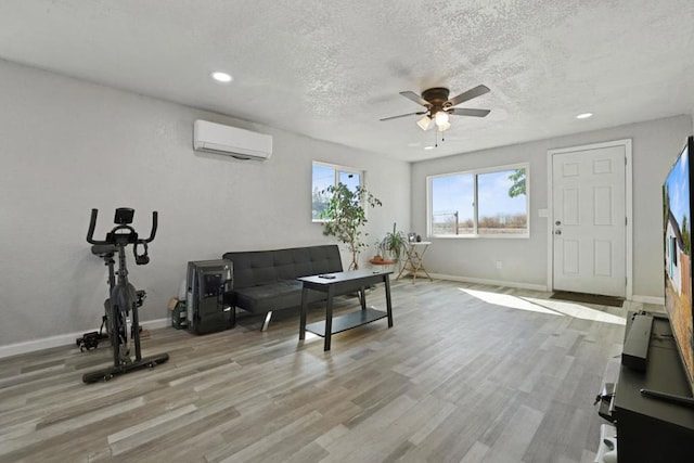 living room with light hardwood / wood-style flooring, a textured ceiling, ceiling fan, and a wall mounted AC