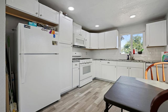 kitchen with dark stone counters, sink, white appliances, and white cabinetry