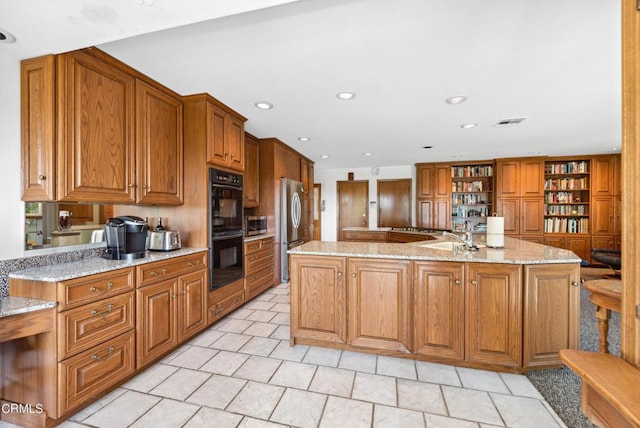 kitchen featuring a center island with sink, light stone counters, stainless steel appliances, and sink