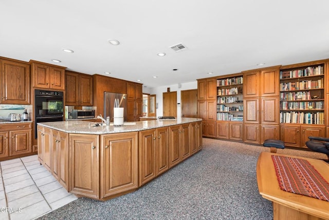 kitchen with a center island with sink, sink, light stone countertops, light colored carpet, and stainless steel appliances