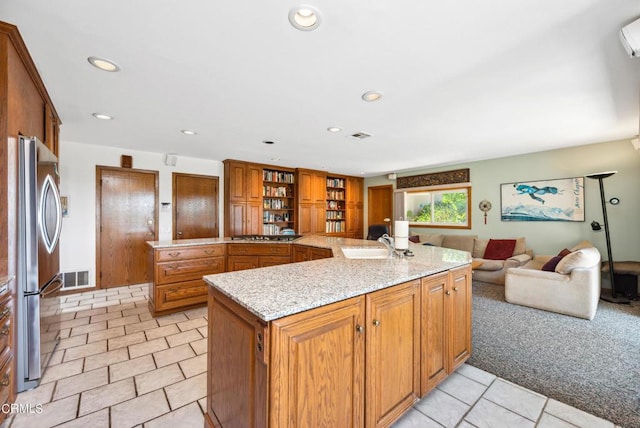 kitchen featuring light stone countertops, sink, light carpet, a center island with sink, and appliances with stainless steel finishes