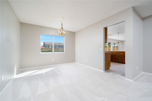 empty room with light colored carpet, a textured ceiling, and a chandelier