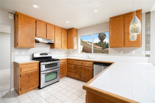 kitchen featuring hanging light fixtures, light tile patterned floors, kitchen peninsula, appliances with stainless steel finishes, and tile counters