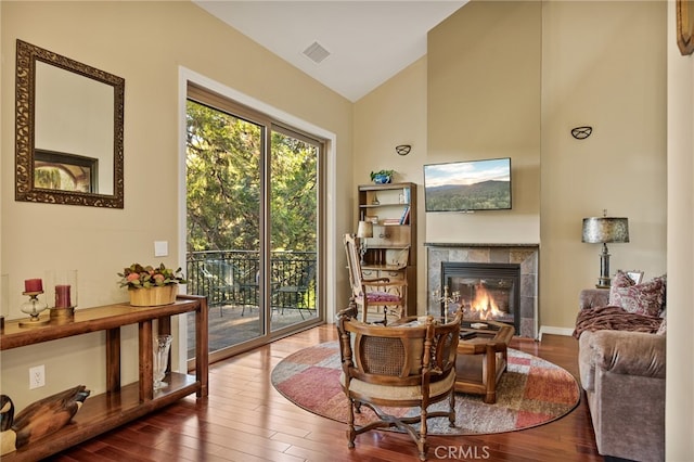 living area featuring wood-type flooring, high vaulted ceiling, and a tile fireplace