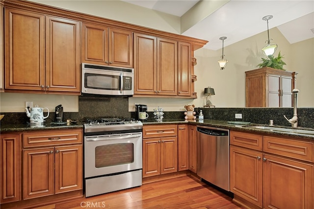 kitchen with appliances with stainless steel finishes, dark stone counters, light wood-type flooring, and decorative light fixtures