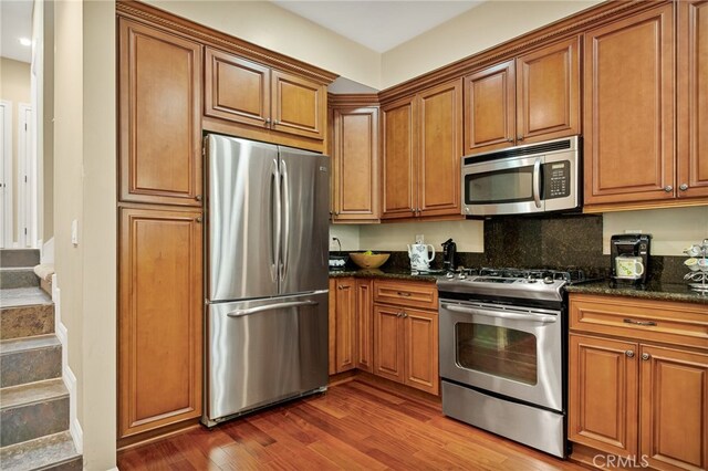 kitchen featuring dark stone countertops, appliances with stainless steel finishes, dark hardwood / wood-style flooring, and decorative backsplash