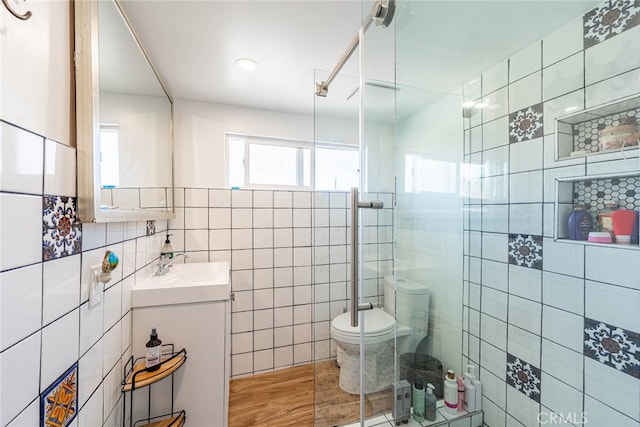 bathroom featuring vanity, wood-type flooring, tile walls, toilet, and a shower with door