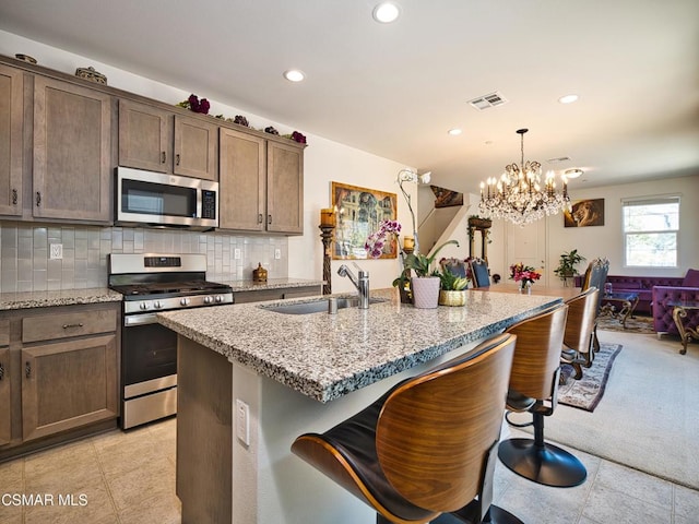 kitchen with a kitchen island with sink, sink, a notable chandelier, stainless steel appliances, and light stone countertops