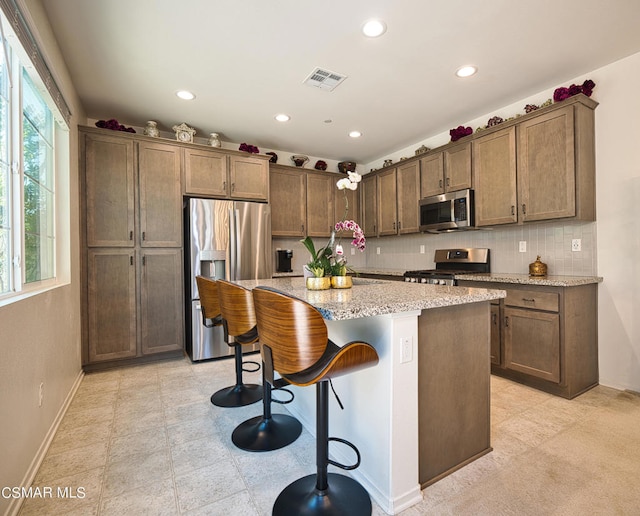 kitchen with appliances with stainless steel finishes, light stone counters, backsplash, a kitchen island, and a breakfast bar area