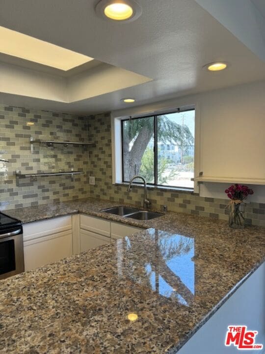 kitchen with decorative backsplash, white cabinetry, dark stone counters, and sink