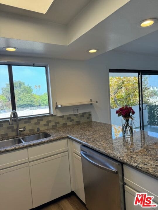 kitchen featuring stainless steel dishwasher, white cabinetry, sink, and a wealth of natural light