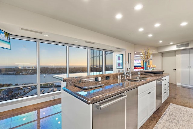 kitchen featuring sink, white cabinetry, a water view, dark stone countertops, and a center island with sink