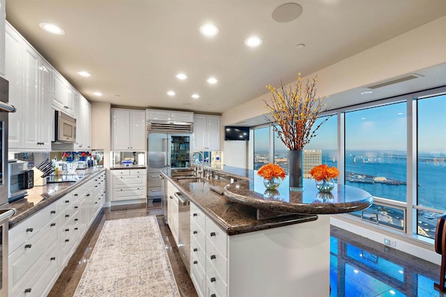 kitchen featuring sink, a spacious island, stainless steel appliances, dark stone counters, and white cabinets