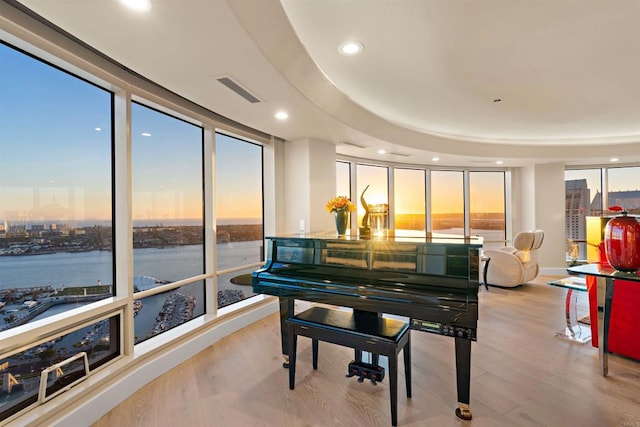 misc room featuring a wall of windows, light hardwood / wood-style flooring, a water view, and a raised ceiling