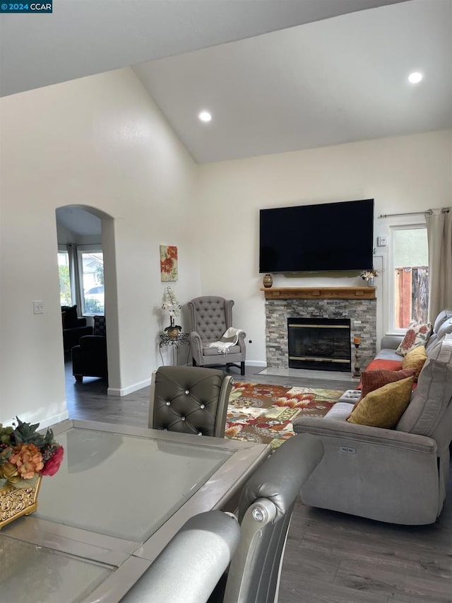 living room featuring a stone fireplace, high vaulted ceiling, and dark wood-type flooring