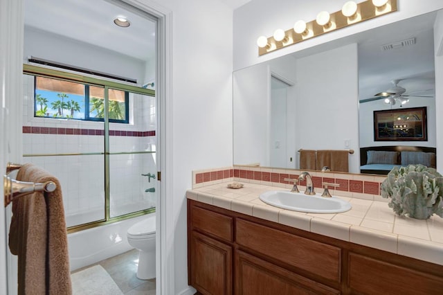 full bathroom featuring toilet, ceiling fan, vanity, tile patterned floors, and enclosed tub / shower combo