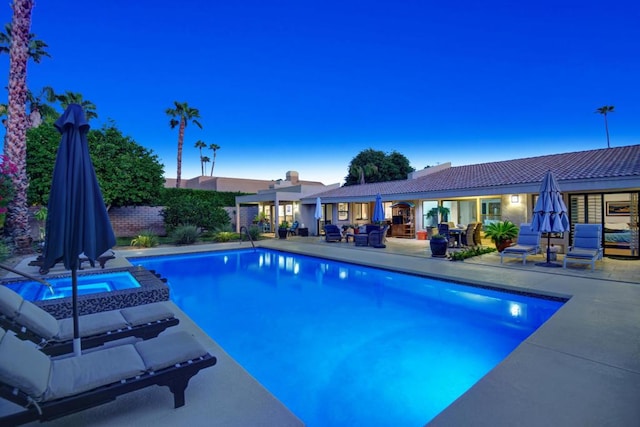 pool at dusk featuring a patio area and an in ground hot tub