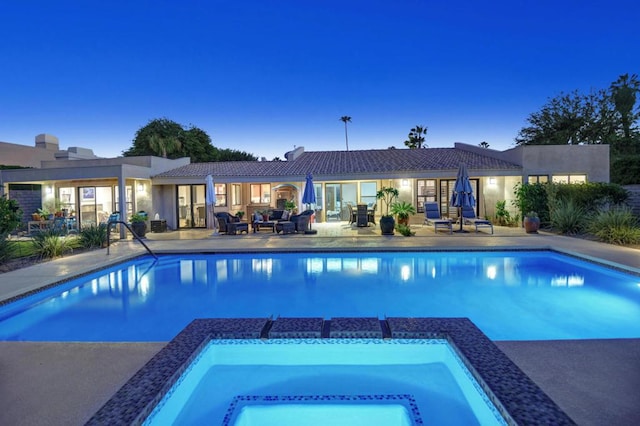 pool at dusk with an in ground hot tub and a patio