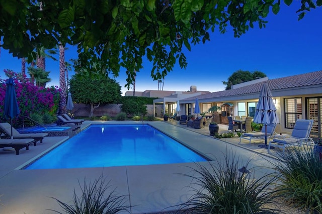 pool at dusk with a patio area and an in ground hot tub