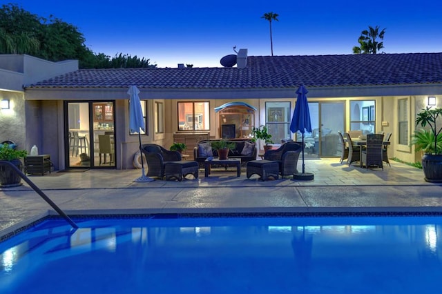 pool at dusk with outdoor lounge area and a patio