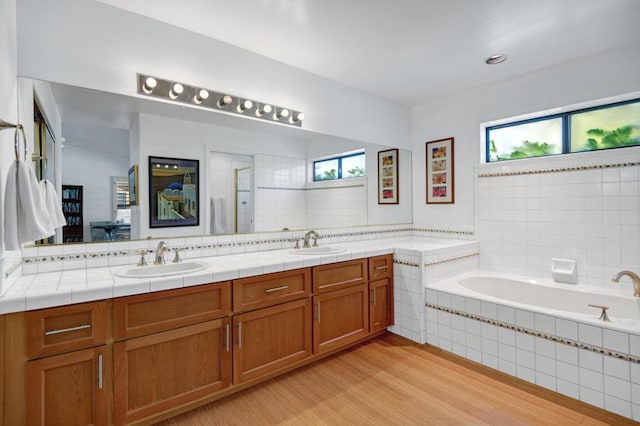 bathroom with hardwood / wood-style flooring, a relaxing tiled tub, and vanity