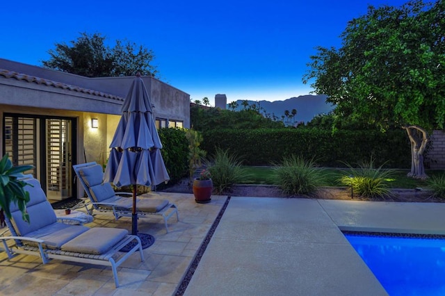 patio terrace at dusk featuring a mountain view and a fenced in pool