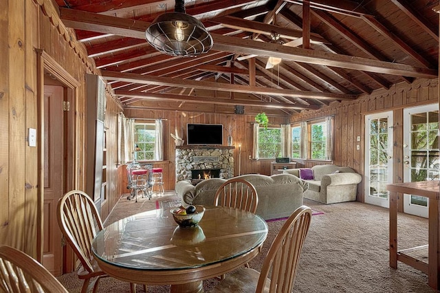 carpeted dining space featuring wood walls, lofted ceiling with beams, and a healthy amount of sunlight