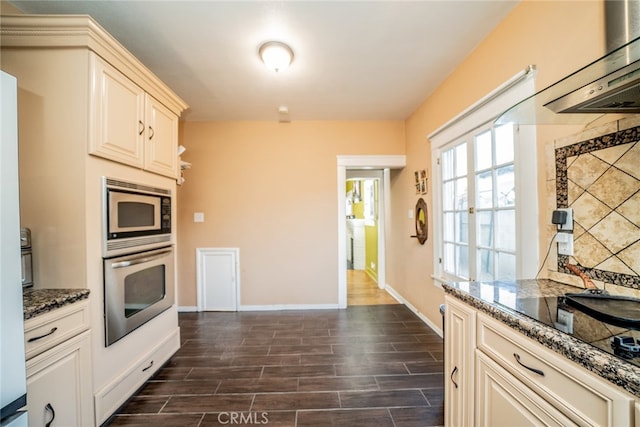 kitchen featuring appliances with stainless steel finishes, cream cabinetry, dark stone countertops, and dark hardwood / wood-style flooring