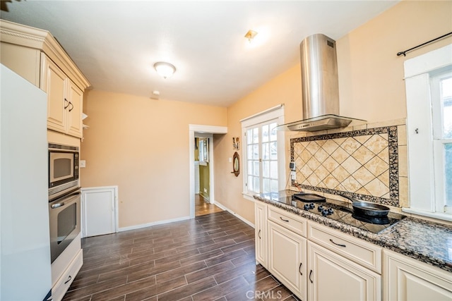 kitchen with dark stone counters, stainless steel appliances, dark wood-type flooring, and wall chimney range hood