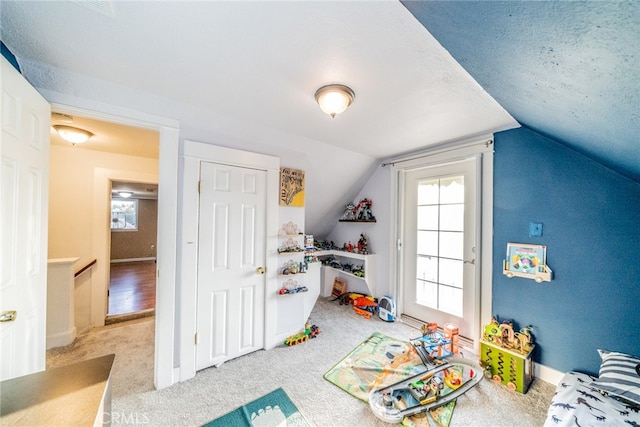 recreation room with a textured ceiling, vaulted ceiling, and light colored carpet