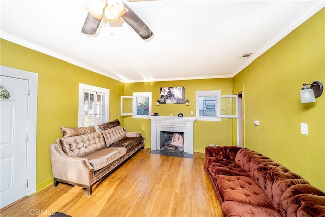 living room with ornamental molding, light wood-type flooring, ceiling fan, and a fireplace