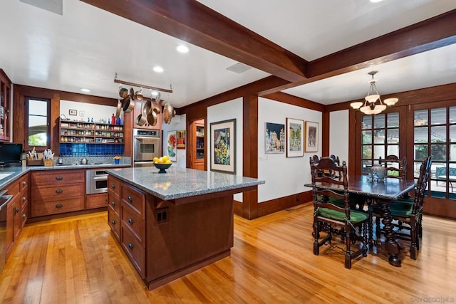 kitchen featuring hanging light fixtures, light wood-type flooring, stone counters, a center island, and a notable chandelier