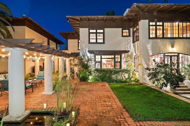 back house at twilight with a yard, a pergola, and a patio area