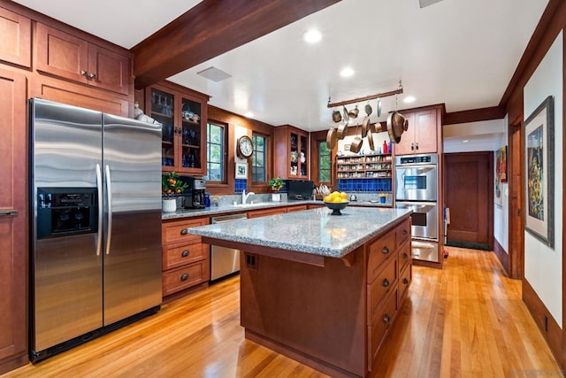 kitchen with light wood-type flooring, stainless steel appliances, a center island, light stone countertops, and a kitchen bar