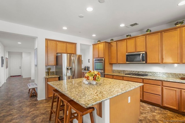 kitchen featuring light stone counters, appliances with stainless steel finishes, a center island, and a kitchen bar