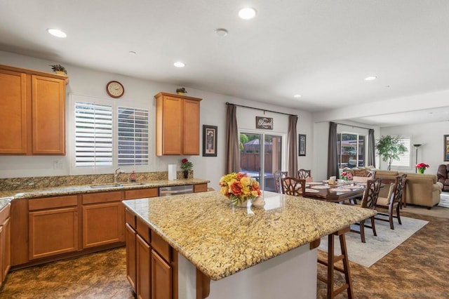 kitchen featuring a kitchen island, dishwasher, sink, light stone countertops, and a breakfast bar