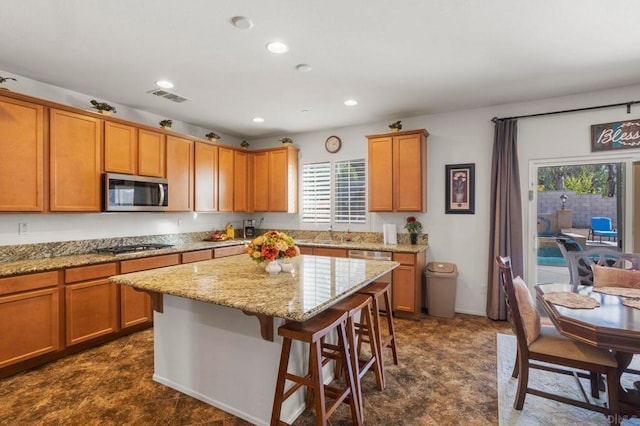 kitchen with a breakfast bar area, light stone countertops, stainless steel appliances, sink, and a center island