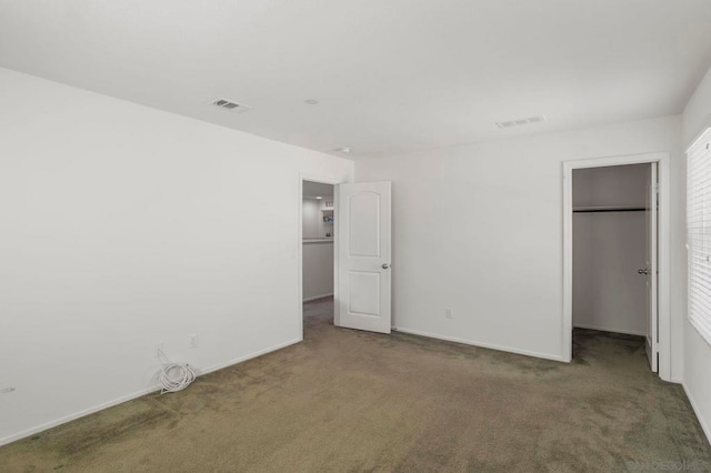 unfurnished bedroom featuring a closet, dark carpet, and a walk in closet