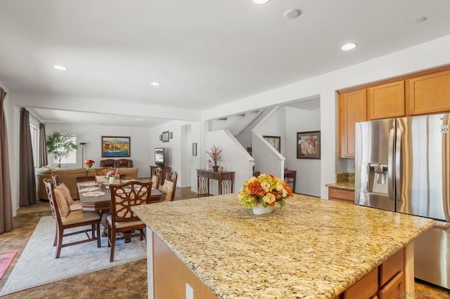 kitchen with a center island, stainless steel fridge with ice dispenser, and light stone counters